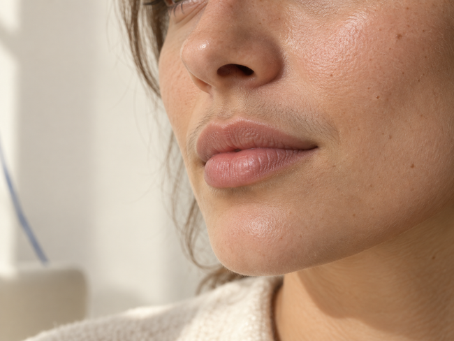 Femme adulte de profil avec de fins poils visibles au-dessus de la lèvre sous une lumière naturelle latérale.
